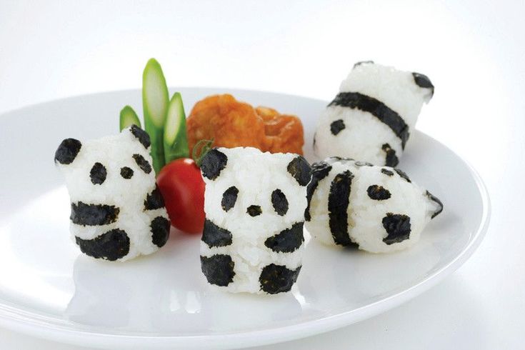 Four pandas made of white rice and seaweed sit on a plate with vegetables.