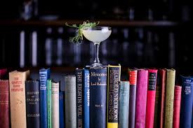 A garnished beverage in a coupe glass sita atop a row of colorful books.