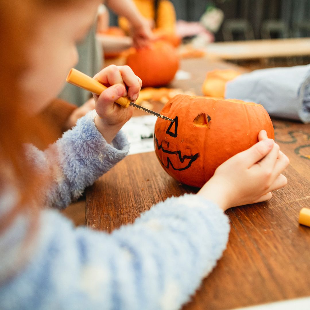 A child carving a small pumpkin with a plastic carving tool is depicted.
