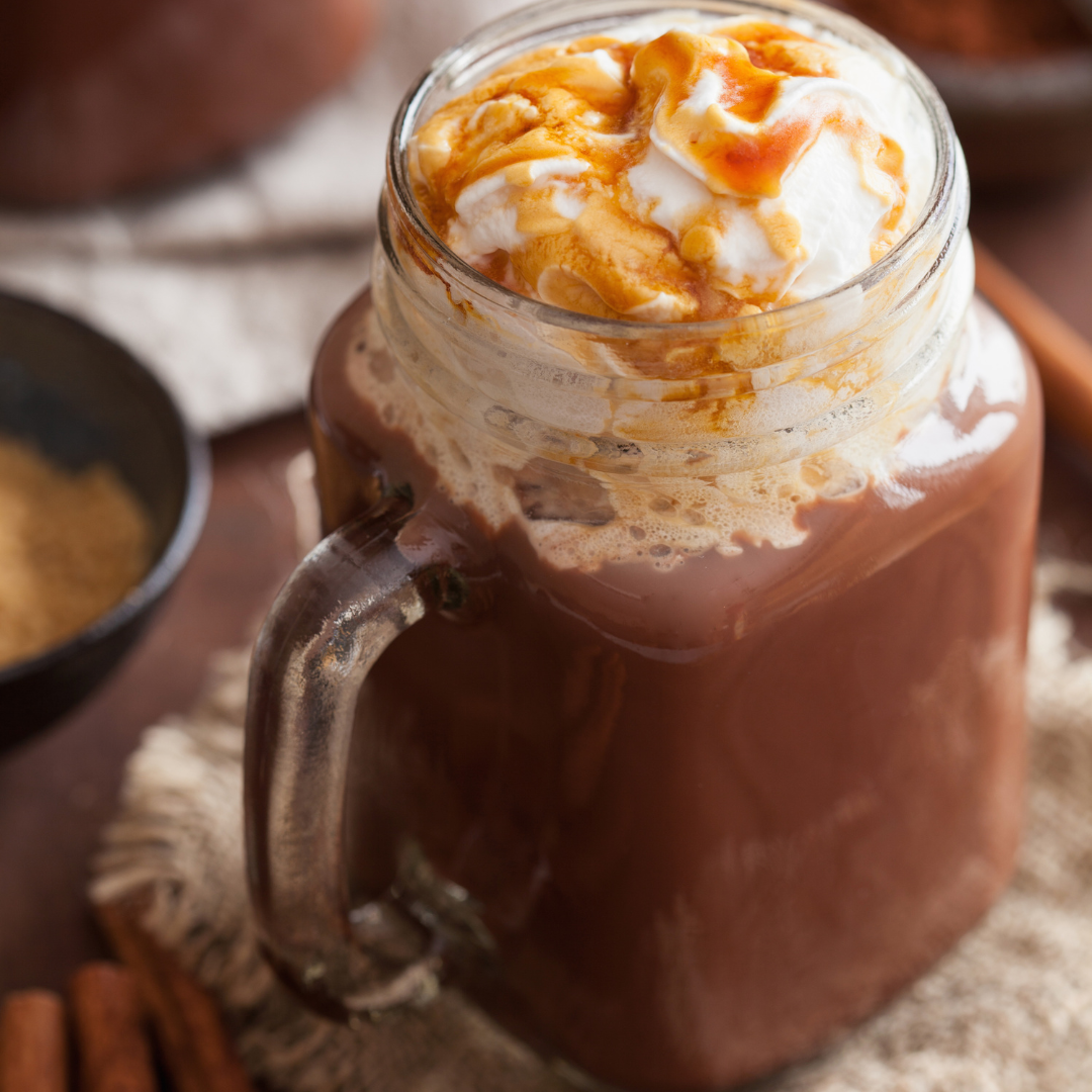A mug of hot cocoa, topped with whipped cream and a drizzle of caramel.