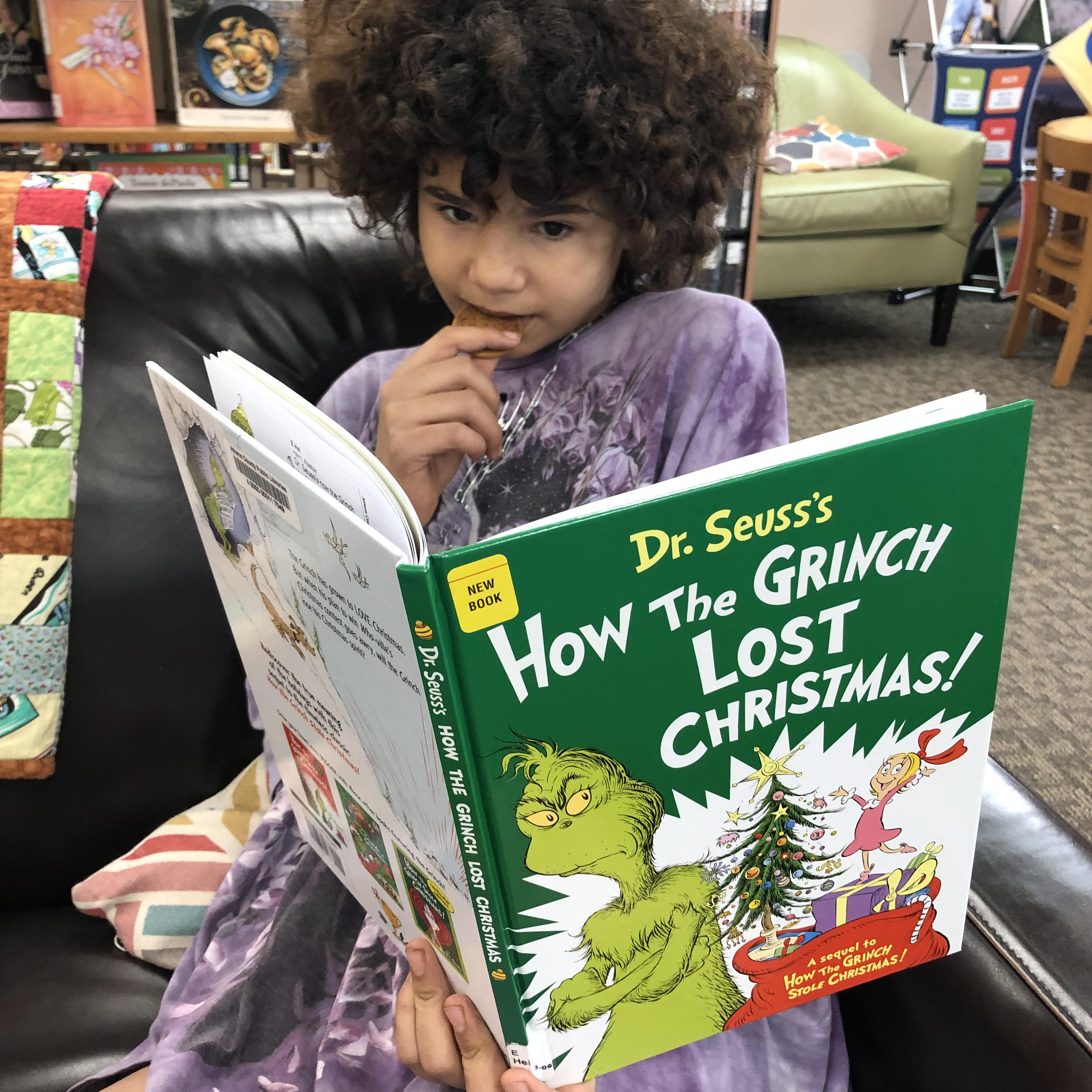 A 10-year-old in a purple shirt eats a cookie and reads "How the Grinch Lost Christmas"
