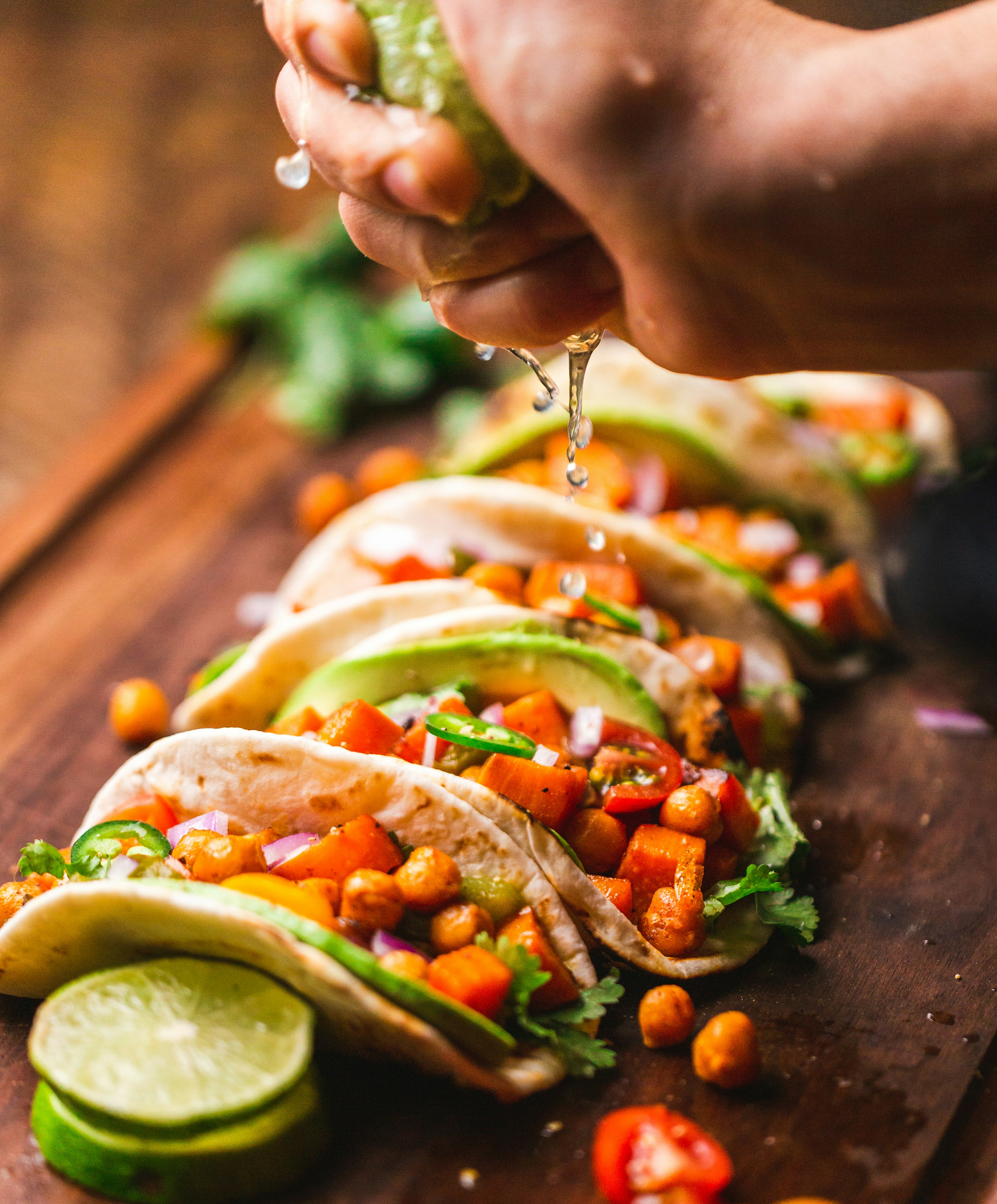 A hand sqeezes a lime over a row of veggie tacos on a wooden slab