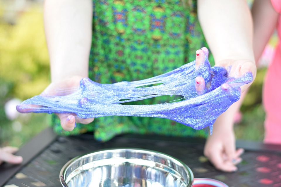 A child's hands stretch sparkly purple slime over a silver bowl.