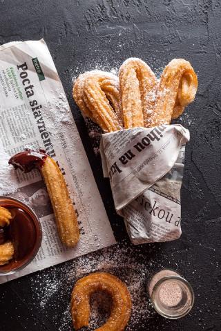Churros wrapped in newspaper with a side of chocolate