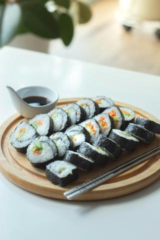Three rows of sushi on a circular wooden tray with a cup of soy sauce or tamari