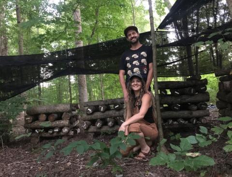 A portrait of the presenters, Anna and Andy with mushroom logs in the forest