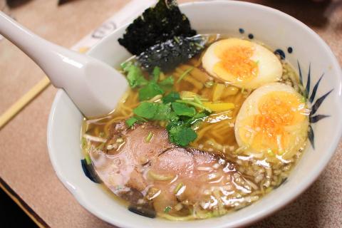 A white spoon in a white bowl which contains broth, ramen noodles, pork, eggs, and seaweed.