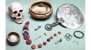 A display of archaeological artifacts - a human skull, a bowl, a hand mirror and several beads - from Birdlip Grave Group site.