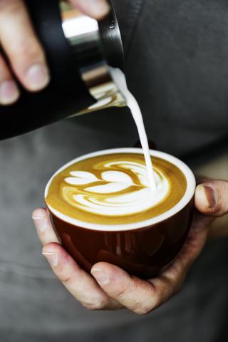 A close up photo of a latte with a barista pouring steamed milk into the cup