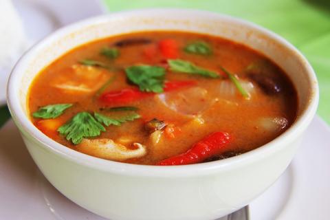 A white bowl of vegetables in a red broth. Cilantro, red bell peppers, and onions are visible.