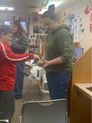 A young library patron pets a turtle who is being held by Jessica of the Hocking College Nature Center