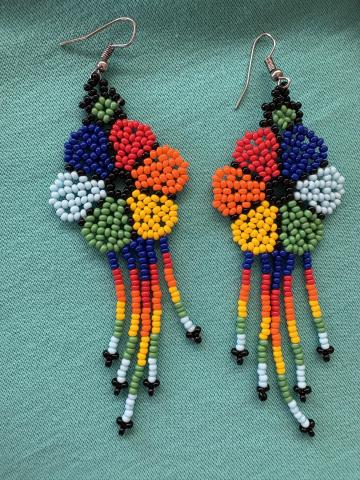 Two huichol style earrings made of small colorful beads on a teal background