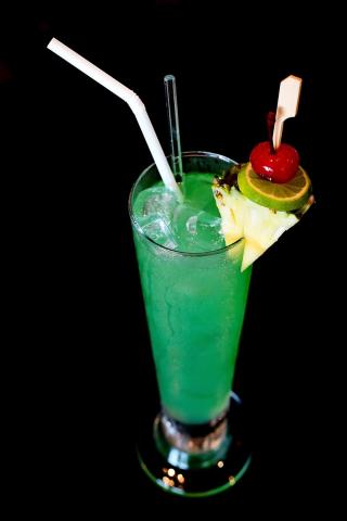 A green beverage in a clear glass with a straw and fruit garnishments