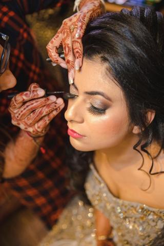 A person with henna art on their hands applies eye makeup to a person in a sequined dress.