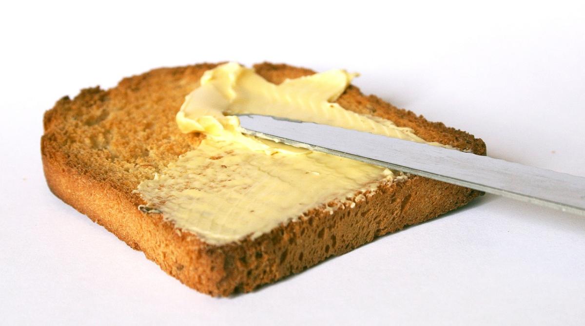 A knife spreading butter on a piece of toast against a white background