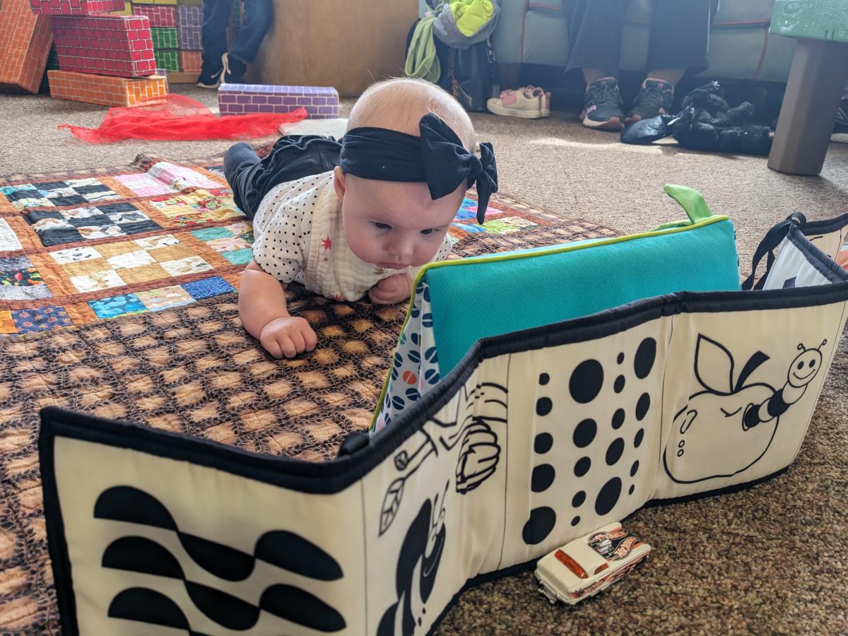 Baby looking at herself while laying on the carpet.