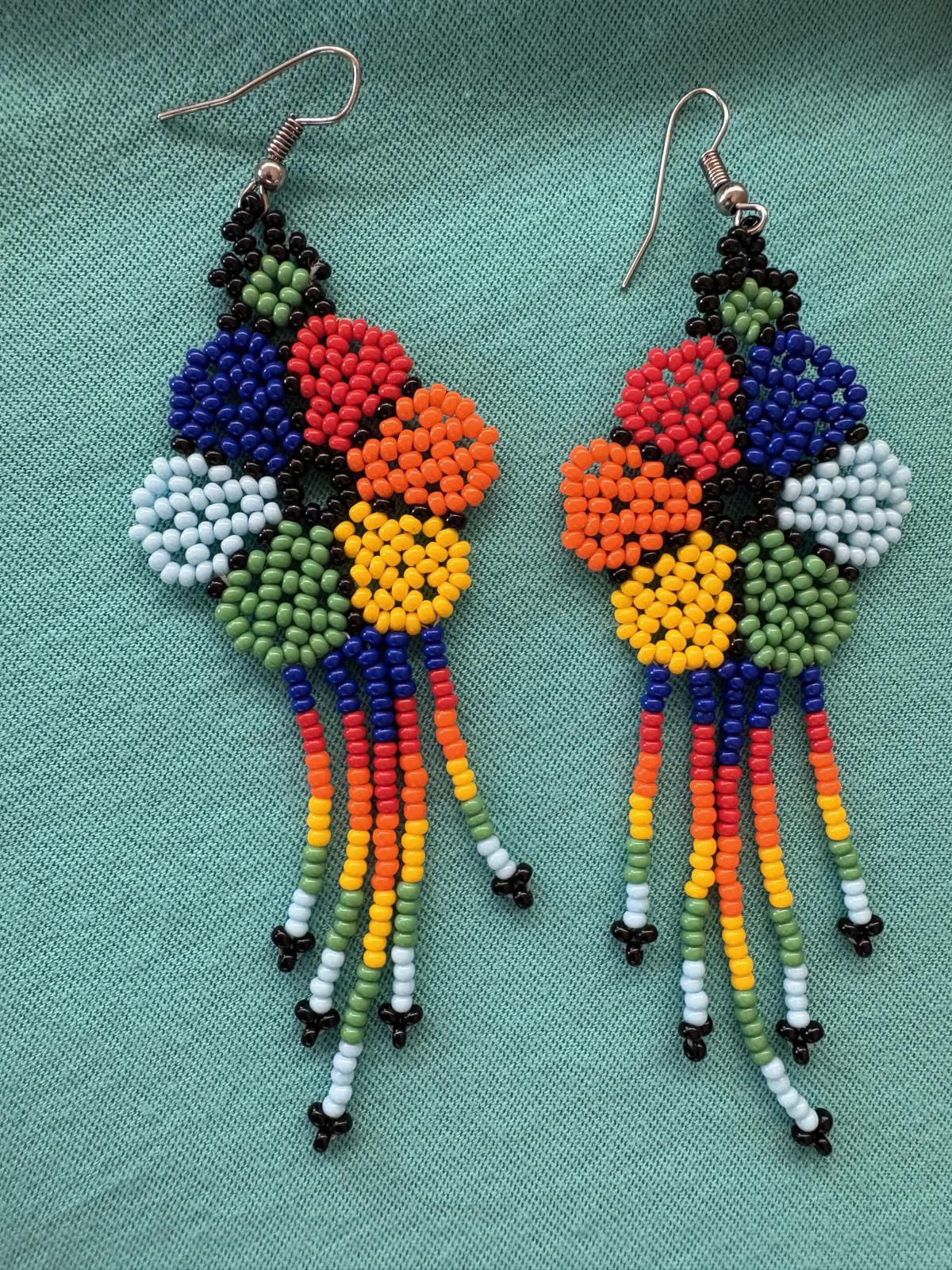 Two huichol style earrings made of small colorful beads on a teal background