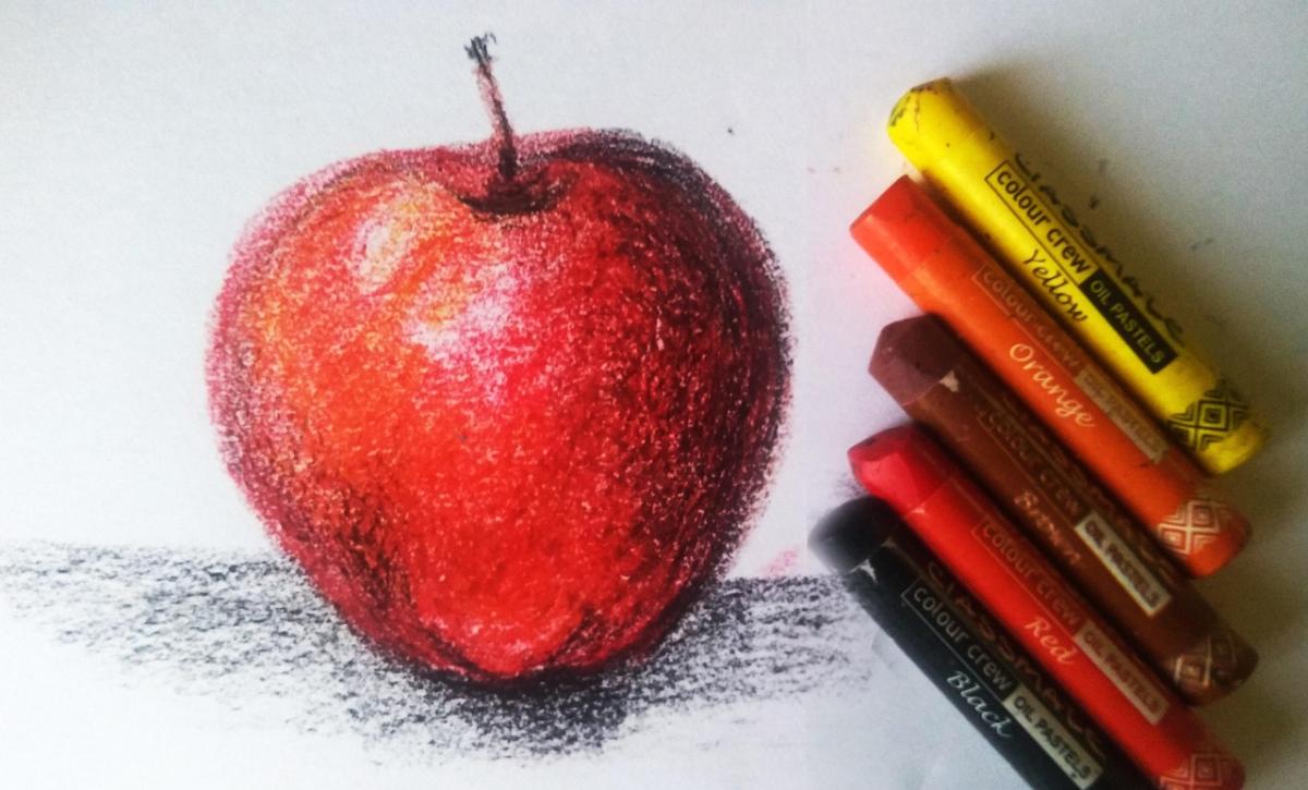 Yellow, orange, brown, red and black pastels next to a pastel drawing of an apple