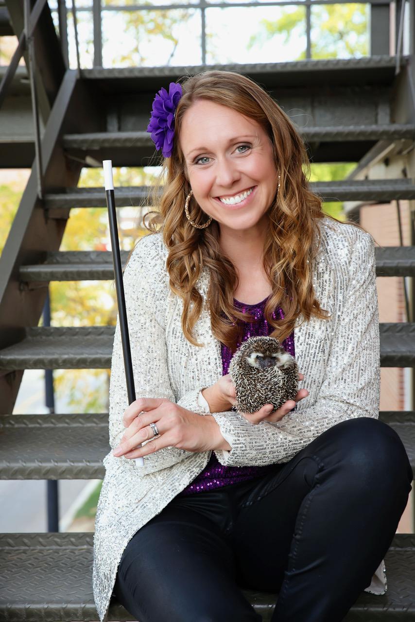 Presenter Erica Carlson sits on some outdoor steps holding a hedgehog and a magic wand.